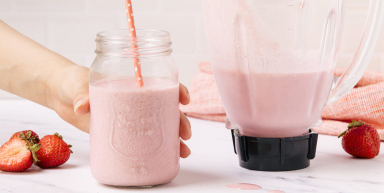 glass and blender of strawberry milkshake on counter