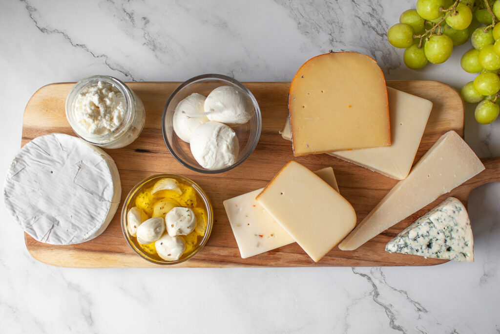 A variety of cheeses on a wood board with a side of grapes