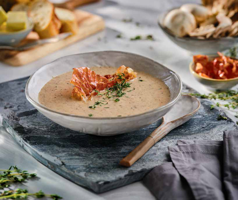 bowl of mushroom soup topped with prosciutto crisps and a side of bread