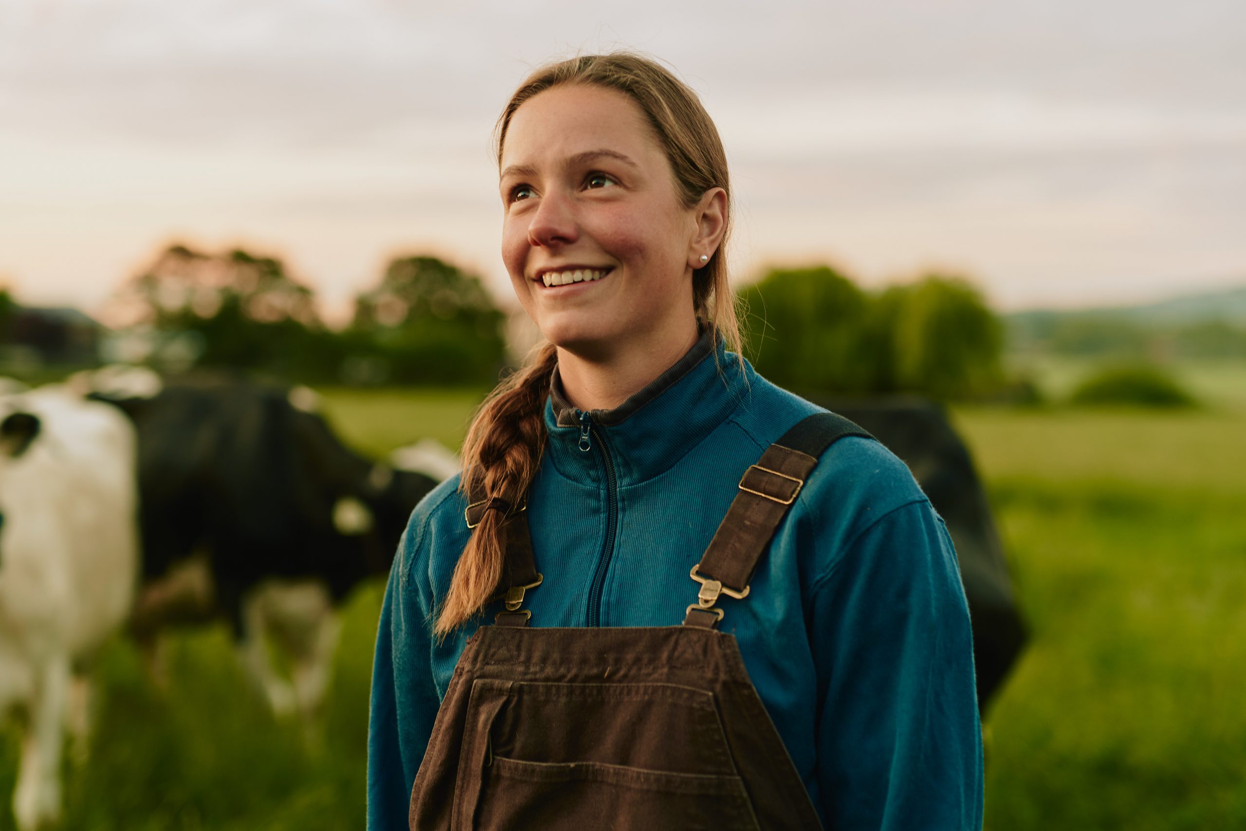 Close up of young woman dairy farmer smiling with a dairy cow in the field