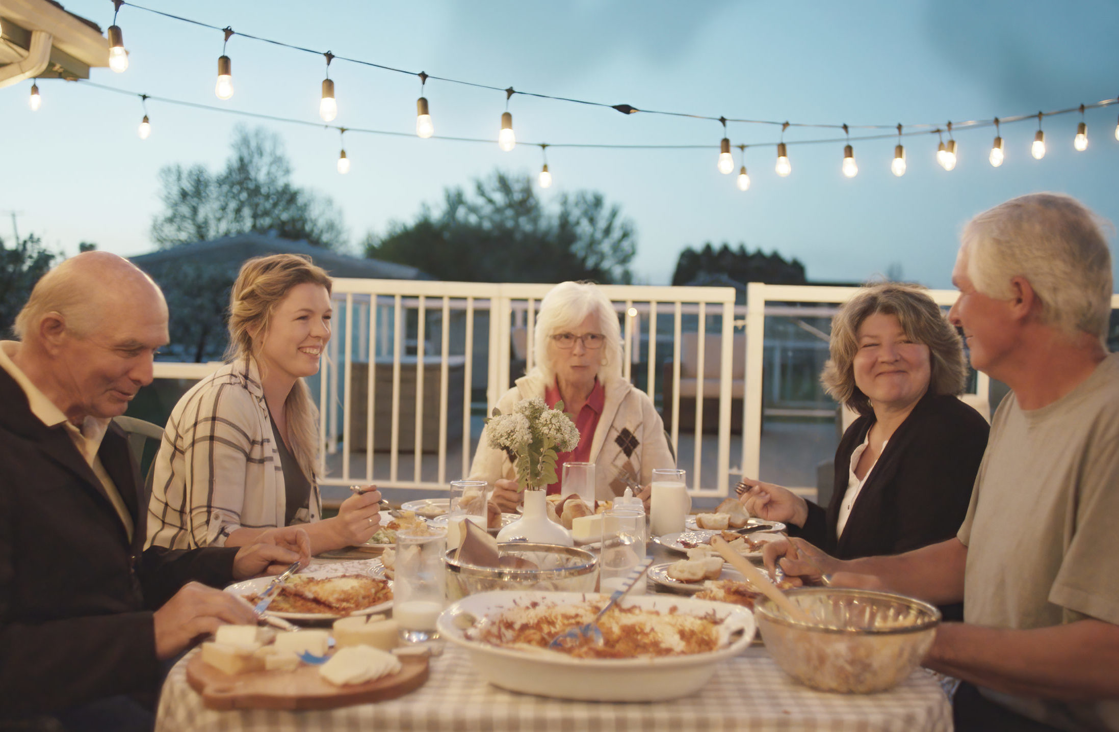 Multi-generational family sitting at an outdoor table in the evening enjoying a meal together