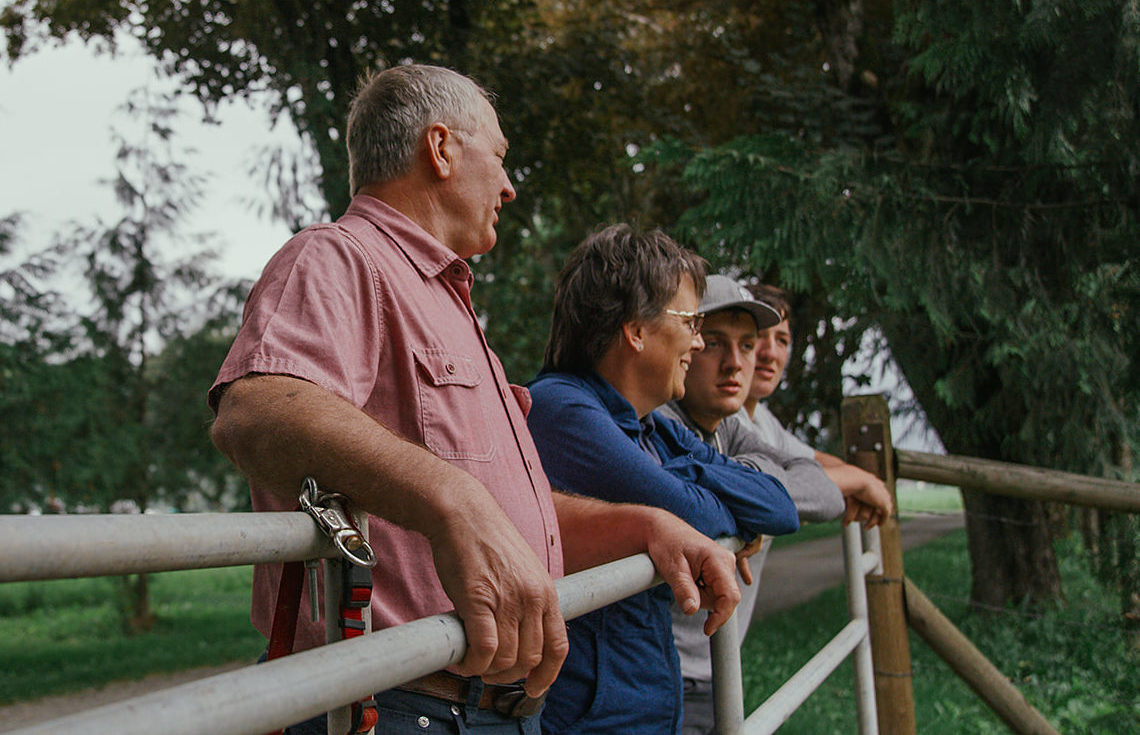 Dairy farming family of four rests on a fence overlooking their farm