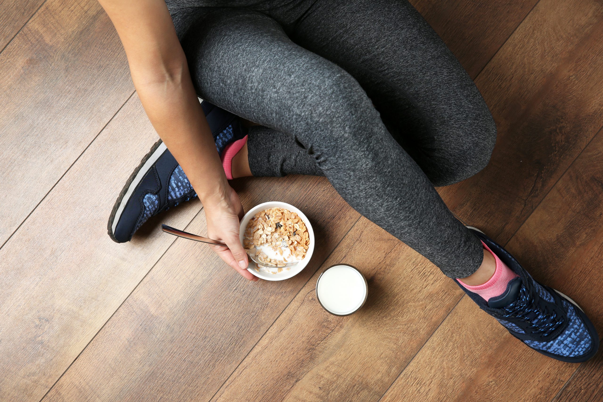 Athlete in leggings and runners sitting beside bowl of cereal with milk