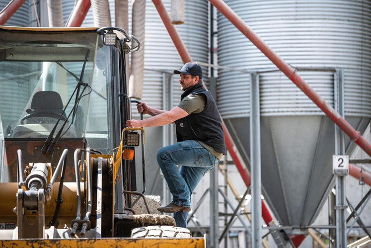 AJ Stobbe entering a loader in front of grain bins. The Stobbe family do as much as they can themselves on-farm, including milling their own grain. 