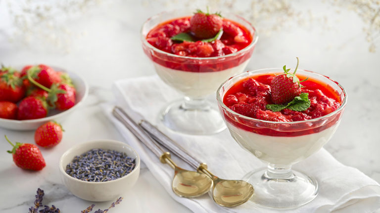 glass bowls filled with strawberry panna cotta with a side of lavender and strawberry garnish