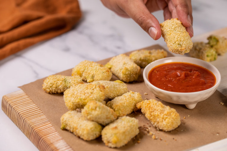 cheese croquettes dipped in marinara sauce on a wooden board