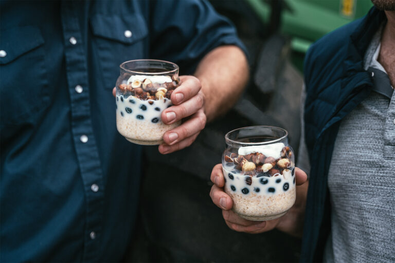 Hands holding glass jars filled with overnight oats and topped with blueberries yogurt and hazelnuts