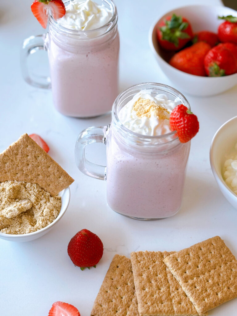 glasses of strawberry cheesecake smoothies with graham crackers and strawberries on the side