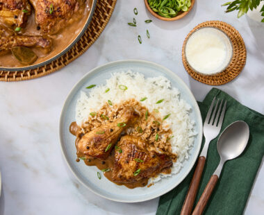 Plate of chicken adobo over rice with a glass of milk and bowl of rice on the side