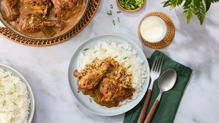 Plate of chicken adobo over rice with a glass of milk and bowl of rice on the side